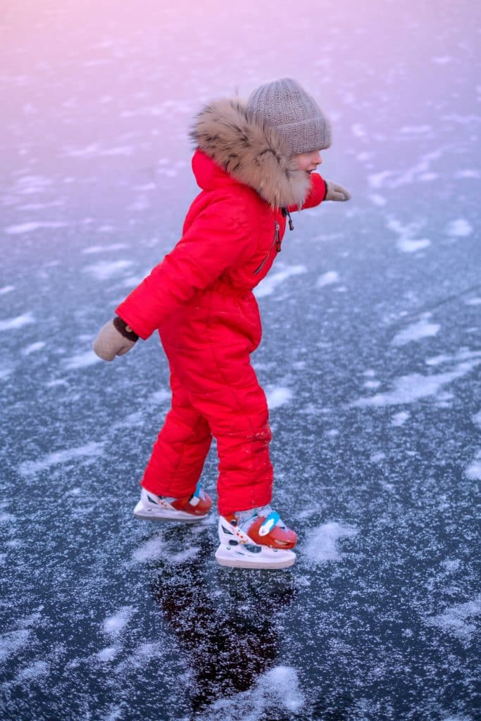 Lapsi luistelee jäällä punaisessa talvihaalarissa